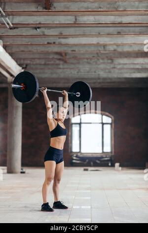 Leistungsstarke Mädchen stehen im Fitnessstudio Heben Schwerhantel über ihren Kopf, Seitenansicht in voller Länge Foto. Kopieren Raum Stockfoto