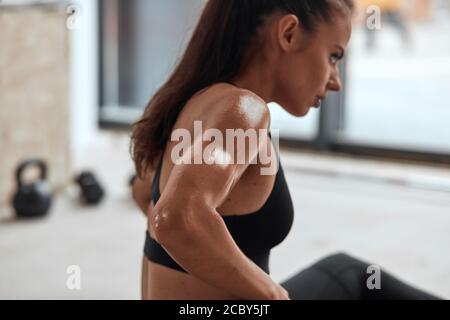 Schwitzen erschöpfte Sportlerin sitzt auf dem Boden im Fitnessstudio nach Fitness-Übungen. Konzept für Erholung und Wohlbefinden. Seitenansicht Stockfoto