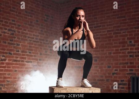 Slim Sport Frau in Sportswear Springen auf fit-Box und Kniebeugen. CrossFit, Bodybuilding. Backwall Hintergrund Stockfoto