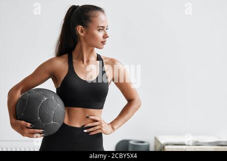 Slim kaukasischen Kreuz fit Frau mit Fitness-Ball Stand in der Turnhalle, Look. Weißer Wandhintergrund Stockfoto