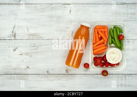 Schulessen - Plastikbox mit Sandwich, Tomaten, Karotten und Karotten Zuckererbsen mit Orangensaft in der Flasche auf weißem Hintergrund. Stockfoto