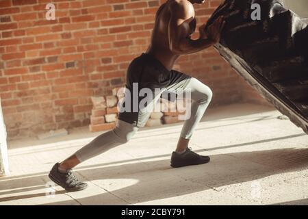 African American crossfit Mann bemüht sich zwar hart mit Hingabe und Entschlossenheit Anheben schwerer Reifen, Training von Kraft und Ausdauer Stockfoto