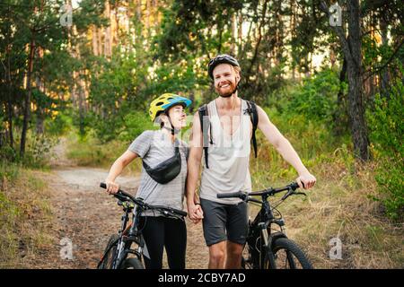 Junge kaukasische Radfahrer gehen und schieben ihre Mountainbikes entlang der Waldstraße im Park. Aktives Sportwochenende. Sportlich schön Stockfoto