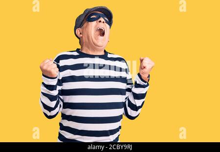 Senior schöner Mann trägt Einbrecher Maske und T-Shirt verrückt und verrückt schreien und schreien mit aggressivem Ausdruck und Arme angehoben. Frustration concep Stockfoto