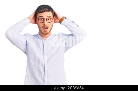Schöner junger Mann mit Bär trägt elegante Business-Shirt und Brille verrückt und verängstigt mit Händen auf dem Kopf, Angst und überrascht von Schock mit offenen m Stockfoto