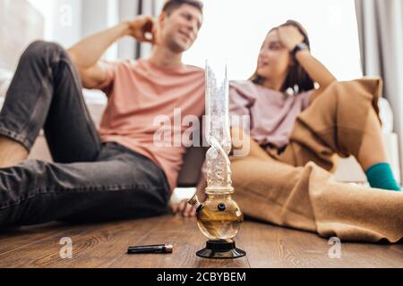 Junge kaukasische Mann und Frau entspannen sich nach der Einnahme von Drogen, Paar fangen ein Summen zu Hause zusammen. Sie sitzen auf dem Boden und verwenden Bong. Marihuana, Cannabis, Stockfoto