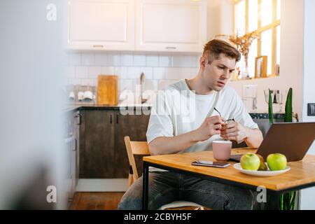 Selbstbewusster kaukasischer Mann arbeiten von zu Hause aus, er verwenden Laptop, bei Freiberufler. Junger Mann sitzen in Hauskleidung und schauen auf Bildschirm von Laptop. Stockfoto