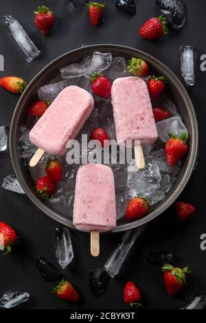 Hausgemachtes Erdbeereis oder Eiszapfen garniert mit Eisstücken und Erdbeerfrüchten mit Blättern, Draufsicht Stockfoto