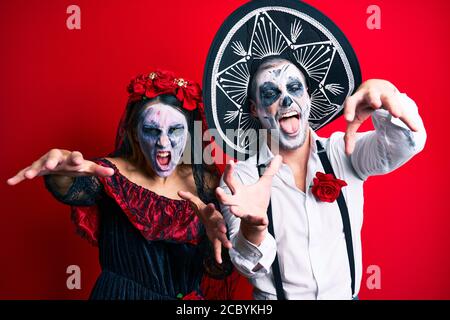 Schönes Paar trägt Tag der Toten Kostüm gestikuliert als Zombie über isolierten roten Hintergrund. Stockfoto