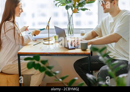 Schöne junge kaukasische Paar verbringen den Morgen anders, Frau machen Make-up vor dem Arbeitstag, während ihr Mann sitzen von zu Hause aus arbeiten, mit Laptop. Stockfoto