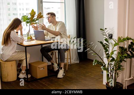 Junge kaukasische Frau verhindert, dass ihr Mann zu Hause arbeiten, Mann sitzen mit Laptop und brüllen Frau, sie weint. Streitereien in der Familie, Arbeit Stockfoto