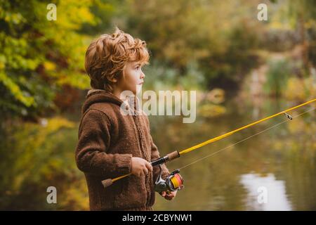 Portrait von glücklichen kleinen Sohn auf dem Fluss mit Spinning Haspel fischen. Happy Kids Herbst Wochenende Konzept. Stockfoto