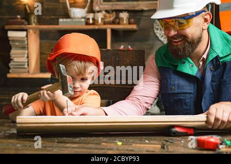 Frühe Entwicklung. Vater und Sohn Junge als Baumeister oder Werkstatt. Vater und Sohn mit Hammer und Nägeln gegen Holzwand. Happy Vatertag Konzept. Kind Stockfoto