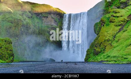 Zwei Touristen stehen während der Sommersaison im Süden Islands am Skogafoss Wasserfall. Stockfoto