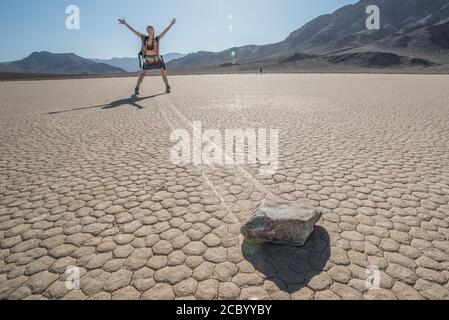 Ein Besucher des Death Valley National Park gibt vor, einen Segelstein zu senden, der über den getrockneten Schlamm der Rennstrecke gleitet. Stockfoto