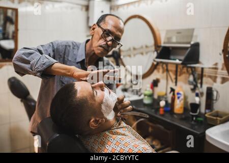 MARRAKESCH, MAROKKO - 10. SEPTEMBER 2019: Mann Rasieren in der traditionellen Straße arabischen Barbershop in Marrakesch. Lokaler Friseur Job in Marokko. Stockfoto