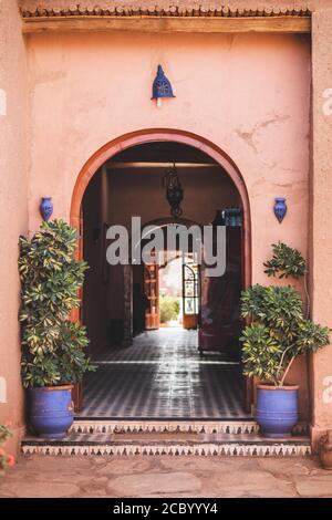 Traditionelle marokkanische Architektur mit roten Terrakotta-Wänden. Bogeneingang, blaue Laternen und Tontöpfe mit Pflanzen. Perspektive innen. Stockfoto