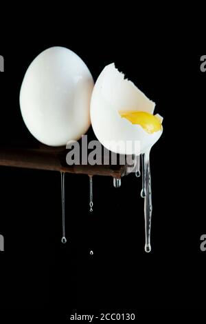 Hühnereier, ein Ei wird gebrochen, in dem das Eigelb sichtbar ist und das Weiß auf einem schwarzen Hintergrund abfließt. Stockfoto