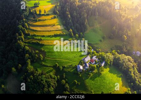 Bukovo, Slowenien - Luftaufnahme eines kleinen Bergdorfes in den slowenischen alpen bei Bukovo an einem sonnigen Sommermorgen. Warme Farben, lange Schatten und V Stockfoto