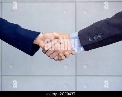Geschäftsmann und Geschäftsfrau schütteln Hände in Bürowand Hintergrund. Handshake zwischen Geschäftsleuten. Teamarbeit, Begrüßung oder Dank Stockfoto
