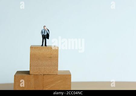 Miniatur Menschen Konzept - ein verzweifelter Geschäftsmann auf Holz stehen Blockdenken nach Lösung Stockfoto