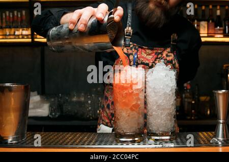 Ein professioneller Barkeeper macht zwei rote Cocktails und gießt einen Cocktail aus einem Shaker. Cocktails gibt es an der Bar. Stockfoto