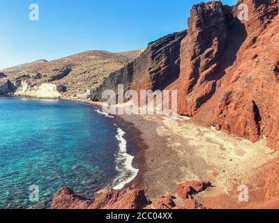 Roter Vulkanstrand in Santorini, Griechenland. Das azurblaue Wasser des Mittelmeers in der Bucht vor der Küste mit Wellen. Stockfoto