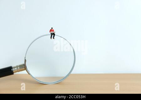 Junger Mann, der auf einer Lupe sitzt, während er ein Buch liest Stockfoto