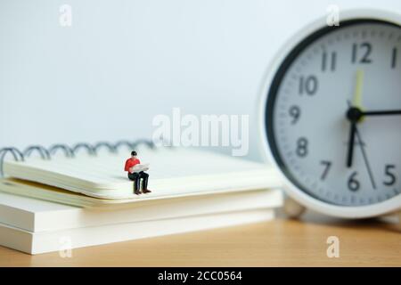 Miniatur Menschen für Morgen Lesung Zeit Konzept - junger Mann Sitzplätze über dem Bücherstapel beim Lesen einer Zeitung Stockfoto