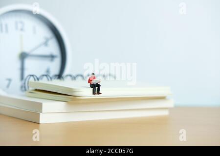 Miniatur Menschen für Morgen Lesung Zeit Konzept - junger Mann Sitzplätze über dem Bücherstapel beim Lesen einer Zeitung Stockfoto