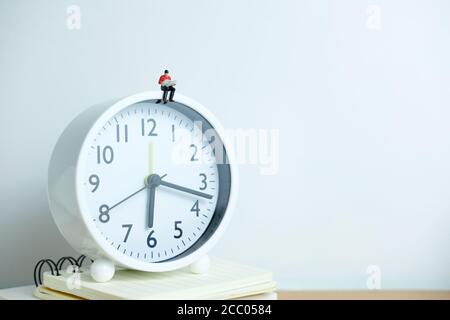 Miniatur Menschen für Morgen Lesung Zeit Konzept - junger Mann Über der Uhr sitzen und ein Buch lesen Stockfoto