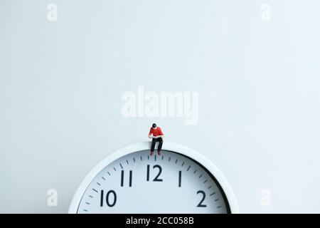 Miniatur Menschen für Morgen Lesung Zeit Konzept - junger Mann Über der Uhr sitzen und ein Buch lesen Stockfoto