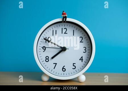 Miniatur Menschen für Morgen Lesung Zeit Konzept - junger Mann Über der Uhr sitzen und ein Buch lesen Stockfoto