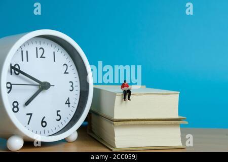 Miniatur Menschen für Morgen Lesung Zeit Konzept - junger Mann Sitzplätze über dem Bücherstapel beim Lesen einer Zeitung Stockfoto