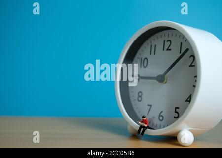 Miniatur Menschen für Morgen Lesung Zeit Konzept - junger Mann Über der Uhr sitzen und ein Buch lesen Stockfoto