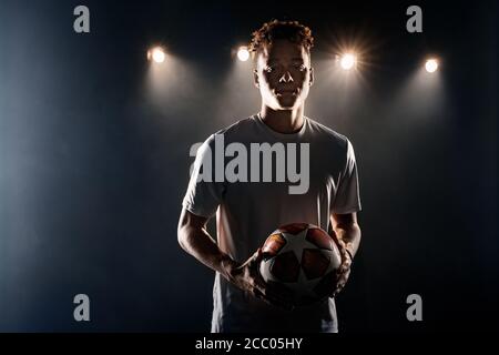 Fußball. Mulatto Kerl stehend isoliert auf dunkel Filed suchen Kamera neugierig Stockfoto