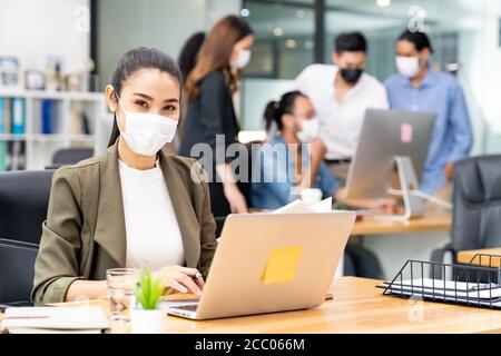 Portrait der asiatischen Büroangestellte Geschäftsfrau tragen Schutzmaske Arbeiten Sie in einem neuen normalen Büro mit interracial Team im Hintergrund Als soziale dist Stockfoto