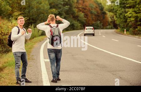 Anreise per Autostop. Hoffnungslos hitchhiker. Männer versuchen stop Auto. Zwillinge zu Fuß entlang der Straße. Wanderer Mann auf der Straße. Art des Reisens. Nur Freunde und Straße voran. das Gefühl der Freiheit. Mit Freunden unterwegs. Stockfoto