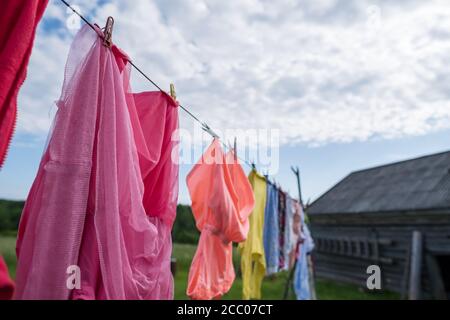 Gewaschene, saubere Kleidung wird im Freien, auf einer Wäscheleine getrocknet und mit Wäscheklammern vor dem Hintergrund einer Scheune gesichert. Stockfoto