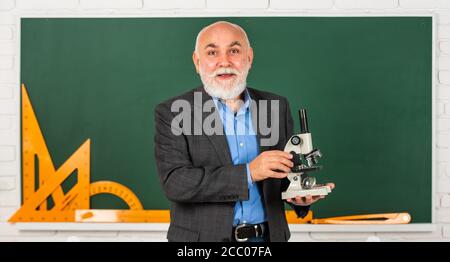Formel. Chemie in der Schule. Wissenschaft Experimente mit Mikroskop im Labor. Biologie Schule Laborausrüstung. Mann im Klassenzimmer mit mathematischen Werkzeugen an der Tafel. Senior Lehrer verwenden Mikroskop. Stockfoto