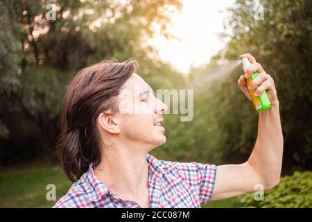 Junger Mann sprüht Moskito Insektenschutz im Wald, Insektenschutz. Ein Mann sprüht Mückenspray auf sein Gesicht. Stockfoto