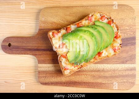 Draufsicht auf einen gegrillten Käse Toast mit Tomaten und Frisch geschnittene reife Avocado auf Holzbrett Stockfoto