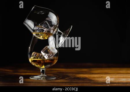 Zwei Whiskey-/Cognac-Gläser mit Eis auf Holzgrund. Dunkler Hintergrund. Stockfoto