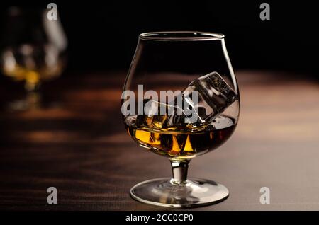 Zwei Whiskey-/Cognac-Gläser mit Eis auf Holzgrund. Dunkler Hintergrund. Stockfoto