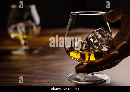 Whiskey / Cognac Glas mit Eis in der Hand auf einem hölzernen Hintergrund. Dunkler Hintergrund. Stockfoto