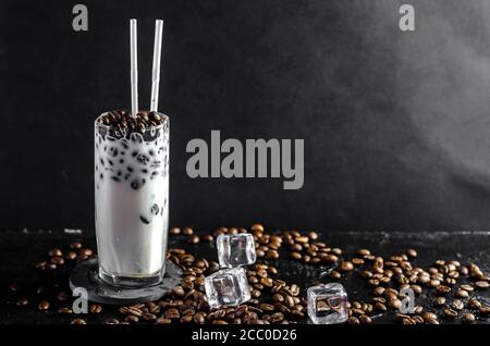 Eiskaffee Frappe mit Milch-Konzept in einem hohen Glas mit den Strohhalmen. Kaffeebohnen auf einem dunklen Hintergrund mit Kopierraum Stockfoto