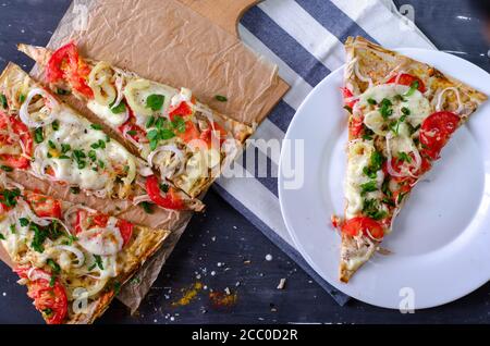 Fladenbrot gesunde Pizzascheiben mit Huhn, Tomaten, Pfeffer, Mozzarella auf einem hölzernen Schneidebrett. Stück Pizza auf einem weißen Teller. Richtige Ernährung Stockfoto