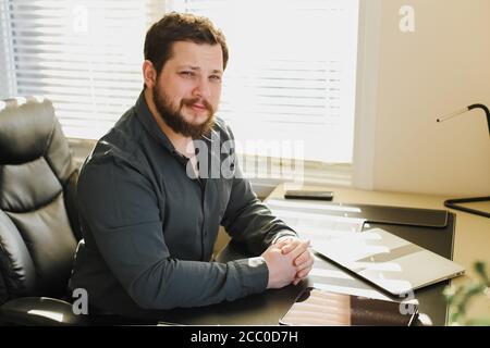 Geschäftsmann sitzt am Schrank mit Dokumenten und Laptop, Tablet auf Tisch. Stockfoto
