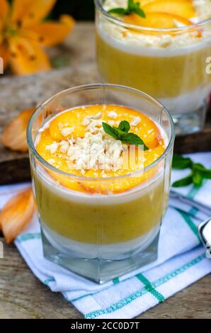 Zwei Galassen Pfirsich-Panna Cotta mit weißen und orangen Schichten. Serviert im Freien auf Holzhintergrund mit Minze und Kirsche. Stockfoto