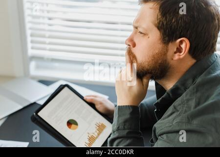 Closeup Denken Ökonom mit Tablette und Blick auf Diagramme mit Diagrammen auf dem Bildschirm. Stockfoto